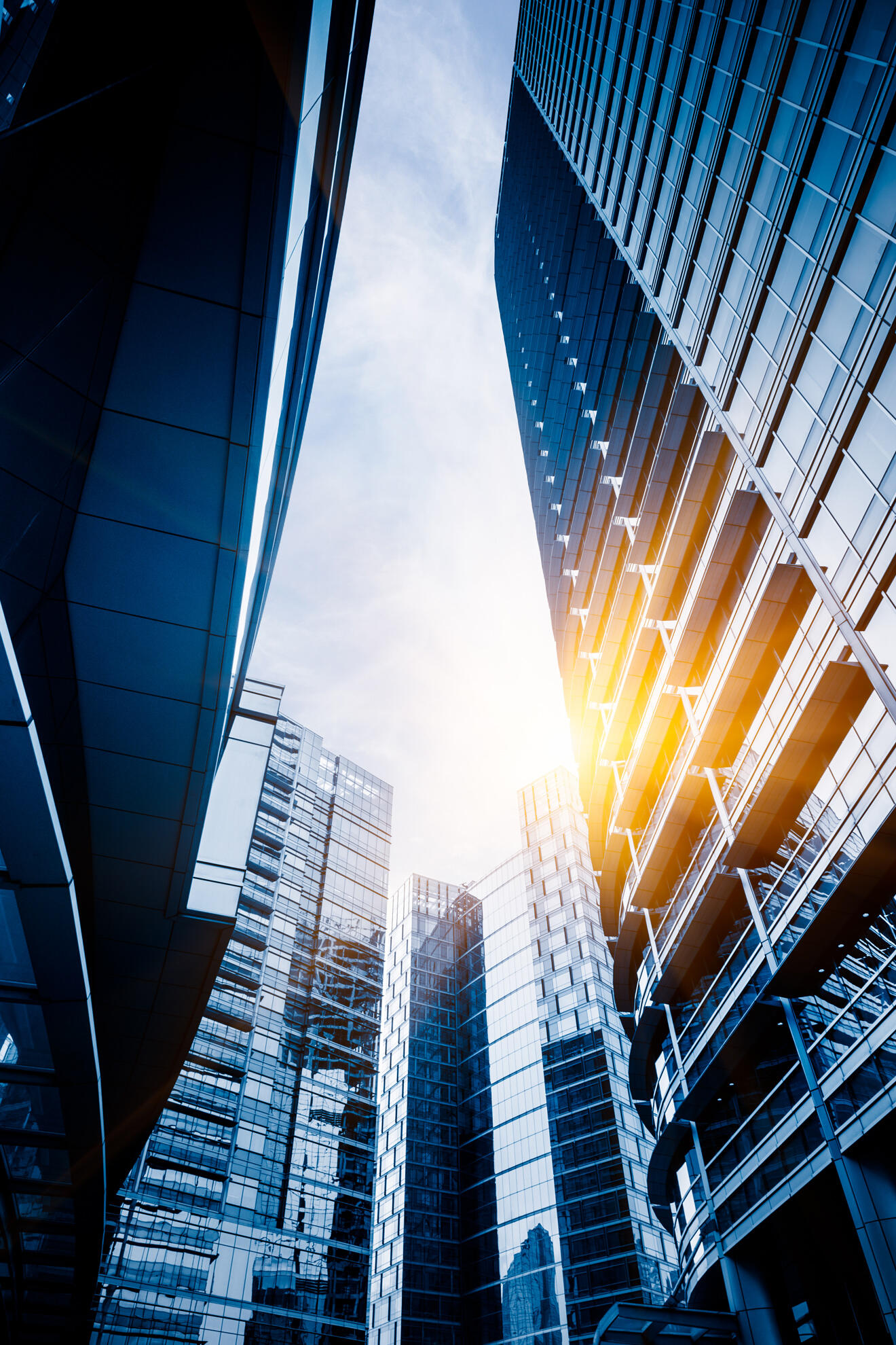 Tall blue glass skyscrapers converge as viewed from a low angle with sunlight flare between them