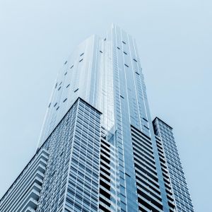 Upward view of a tall modern glass skyscraper with reflective panels against a pale blue sky.