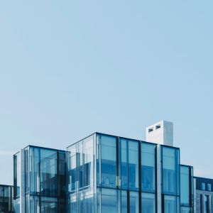 Modern glass office building with blue-tinted windows against a clear blue sky.