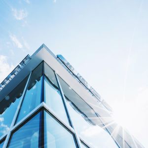 Low-angle view of a modern glass office building with reflective blue windows against a clear sky.