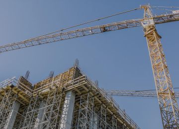 Construction site with a tall crane and metal scaffolding against a clear blue sky.